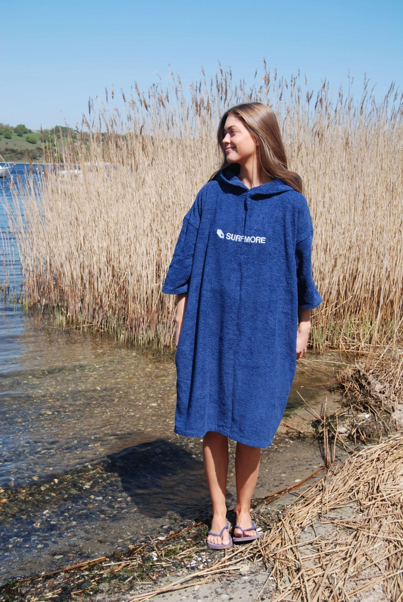 Ung og smilende dame med brunt hår med en badeponcho i blå på